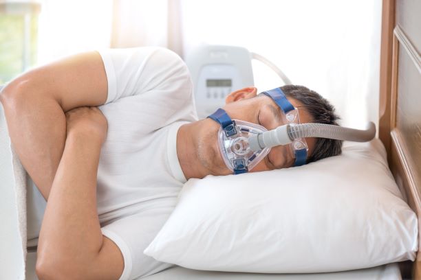 Man liggend in bed met apneu masker en CPAP apparaat op de achtergrond